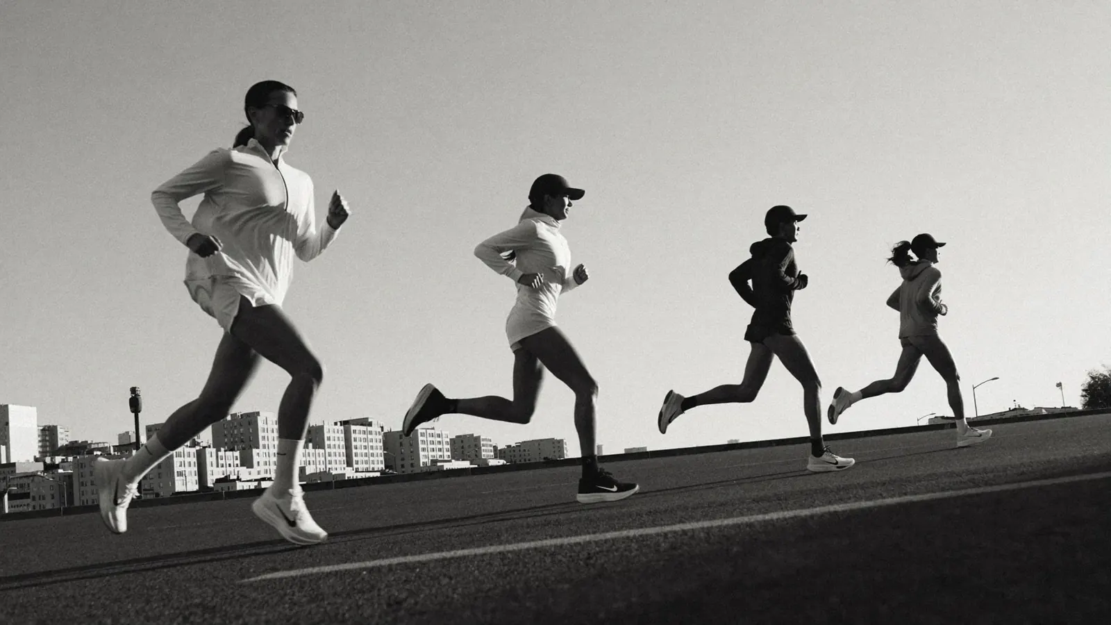 Grupo de corredores en plena zancada sobre una avenida vacía al amanecer, en blanco y negro